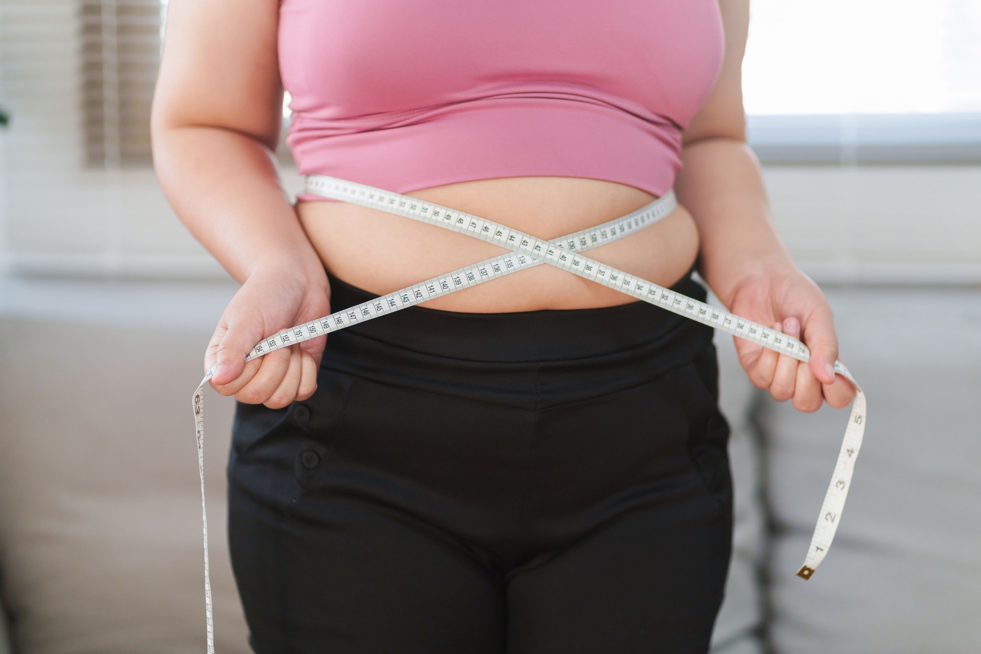 Close up overweight woman measuring her hip with tape measure.