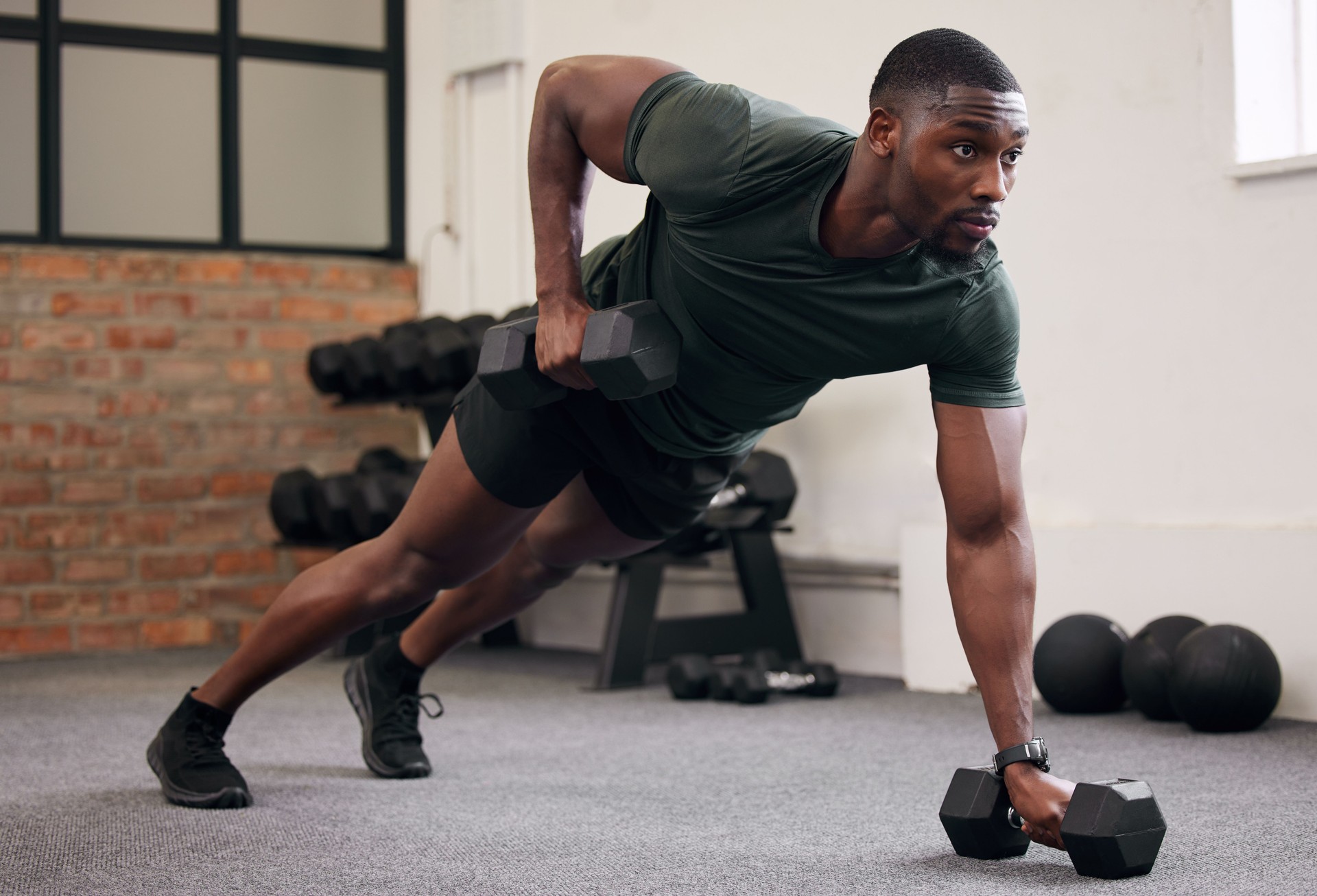 Black man, dumbbell row and training in gym, workout and strong fitness in health club. Serious sports athlete, bodybuilder and weight exercise on ground for energy, power and core strength challenge